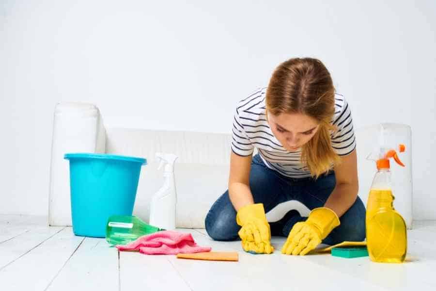 woman surrounded by cleaning supplies scrubbing the floor